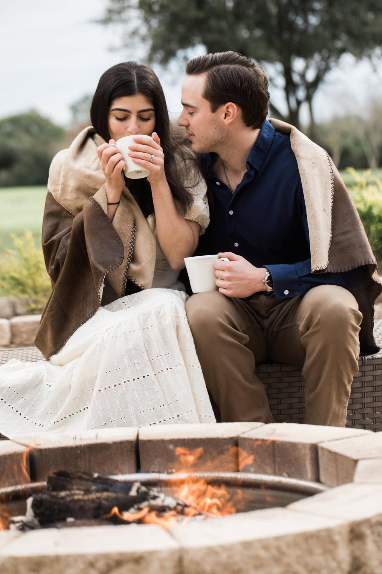 when should you take engagement photos Engaged couple sharing a blanket and warm drinks beside a fire pit during a cool-weather session