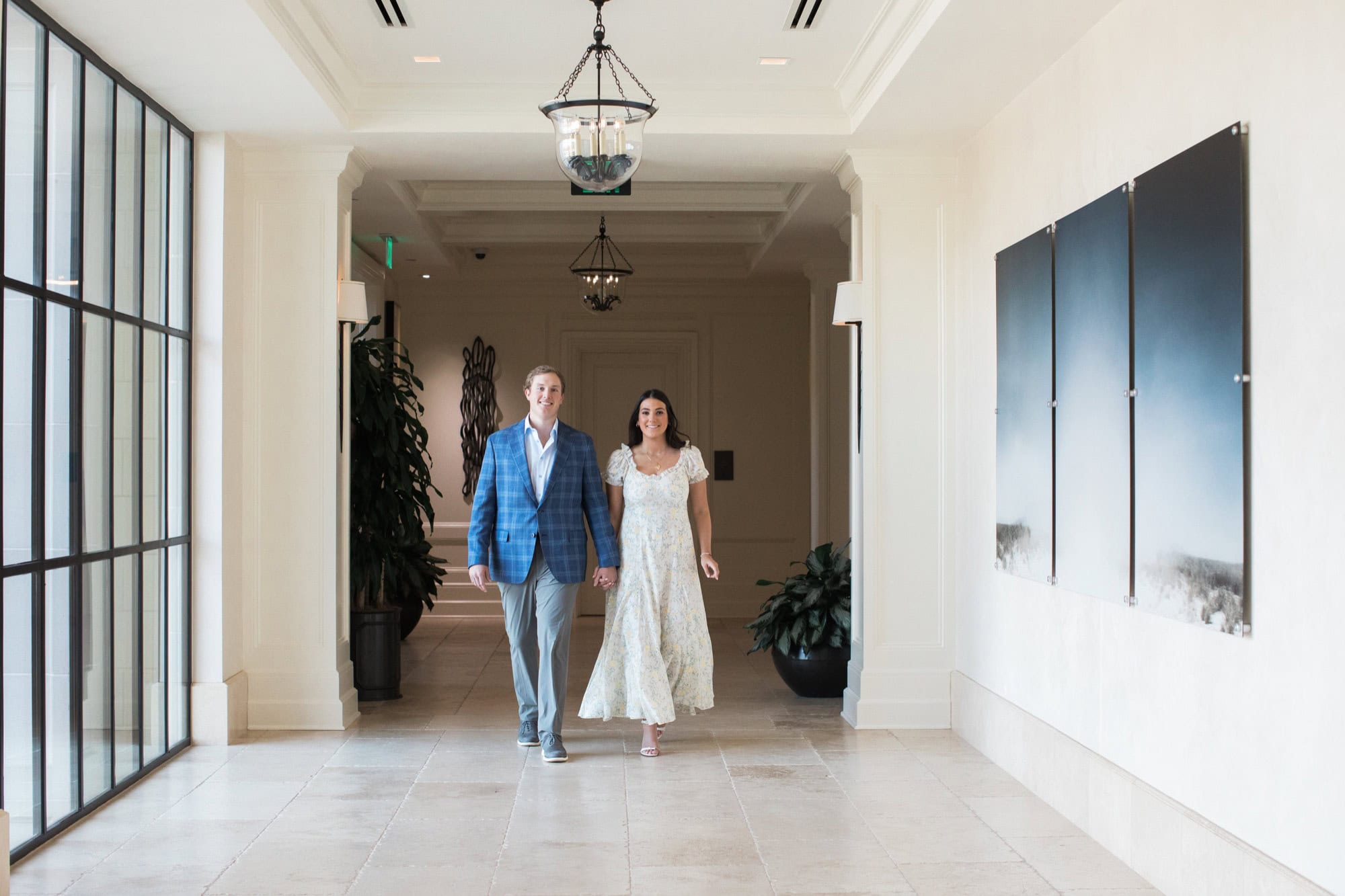 when should you take engagement photos Engaged couple walking through a bright covered corridor in dressy engagement-session outfits