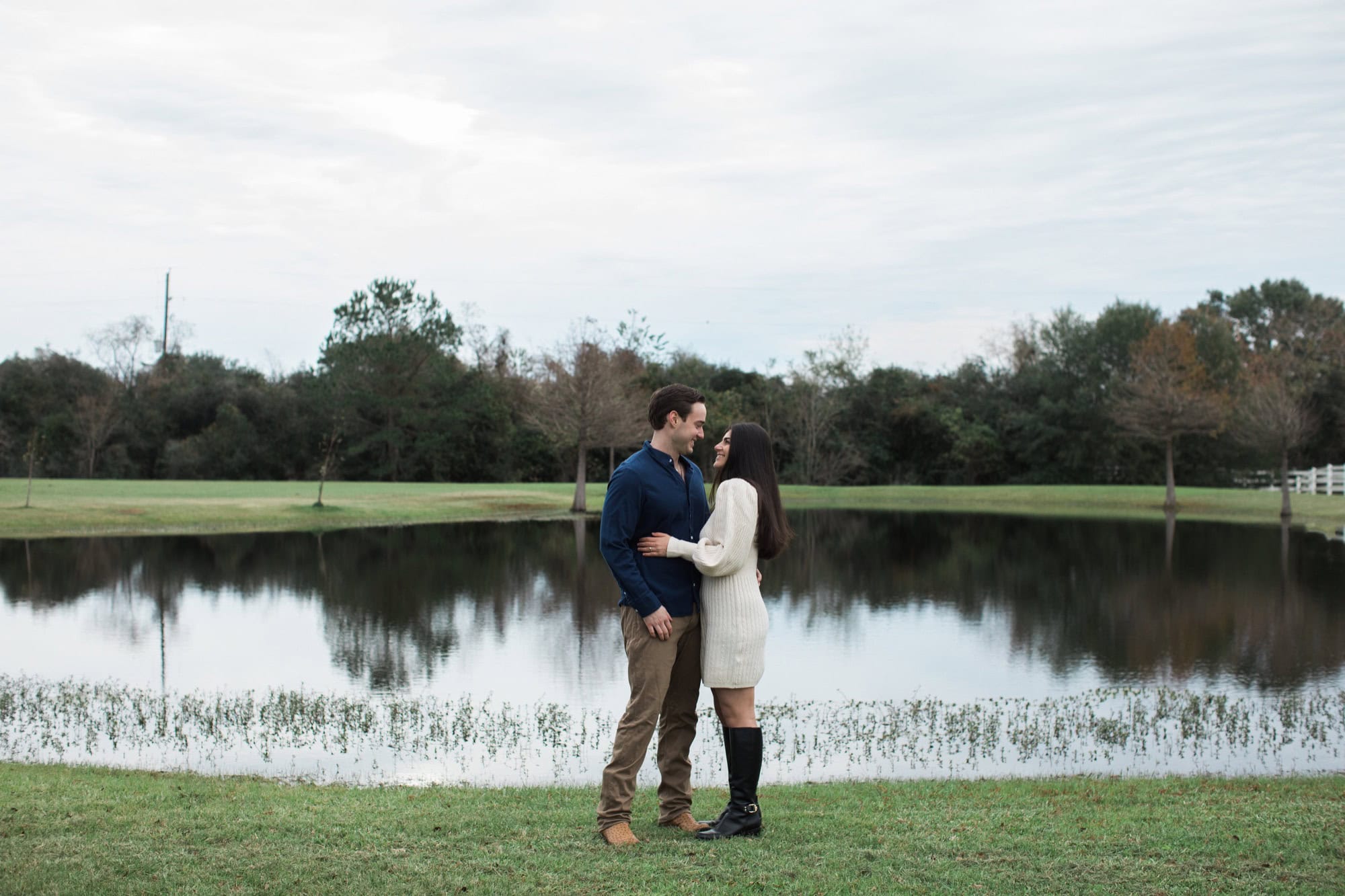 when should you take engagement photos Engaged couple beside a pond in cool-weather outfits under an overcast Houston sky
