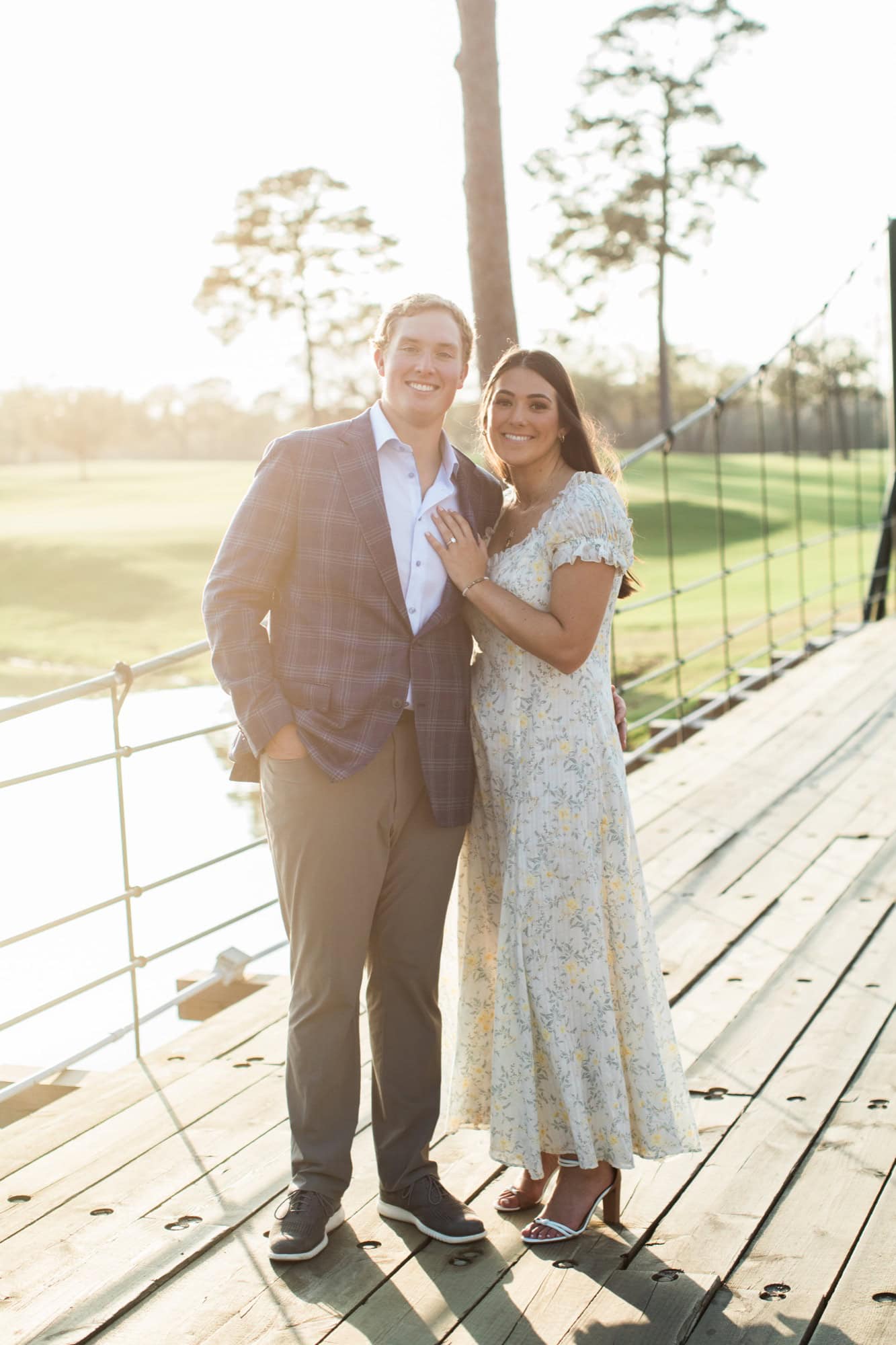 when should you take engagement photos Engaged couple standing on a wooden bridge in warm evening light