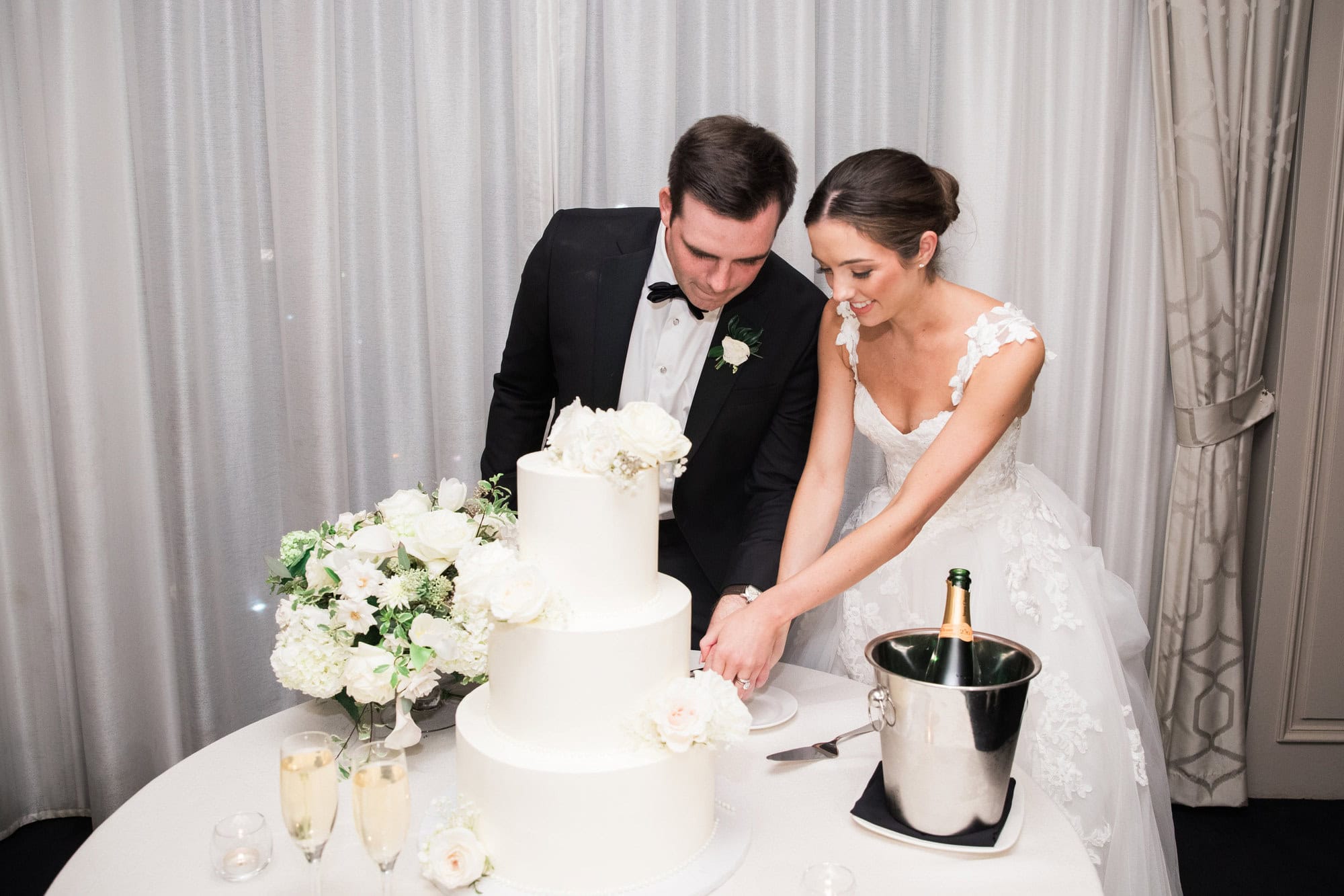 Sydney and Cade cutting their white floral wedding cake.