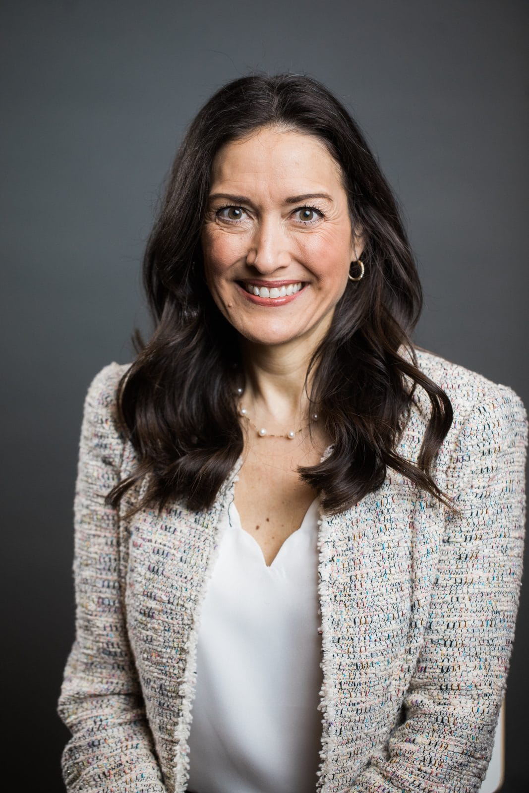 Houston corporate headshots: smiling woman in a tweed blazer on a gray backdrop