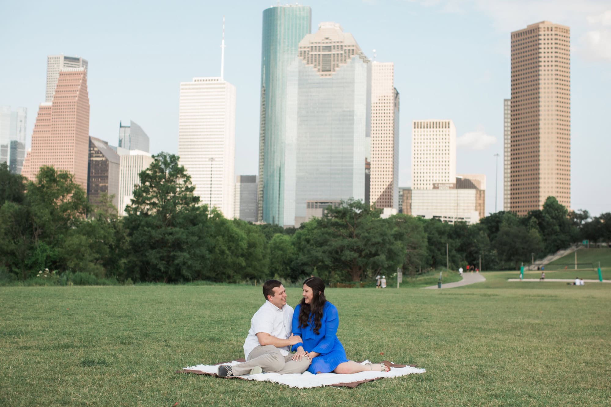 when should you take engagement photos Engaged couple sitting on a picnic blanket with the downtown Houston skyline behind them