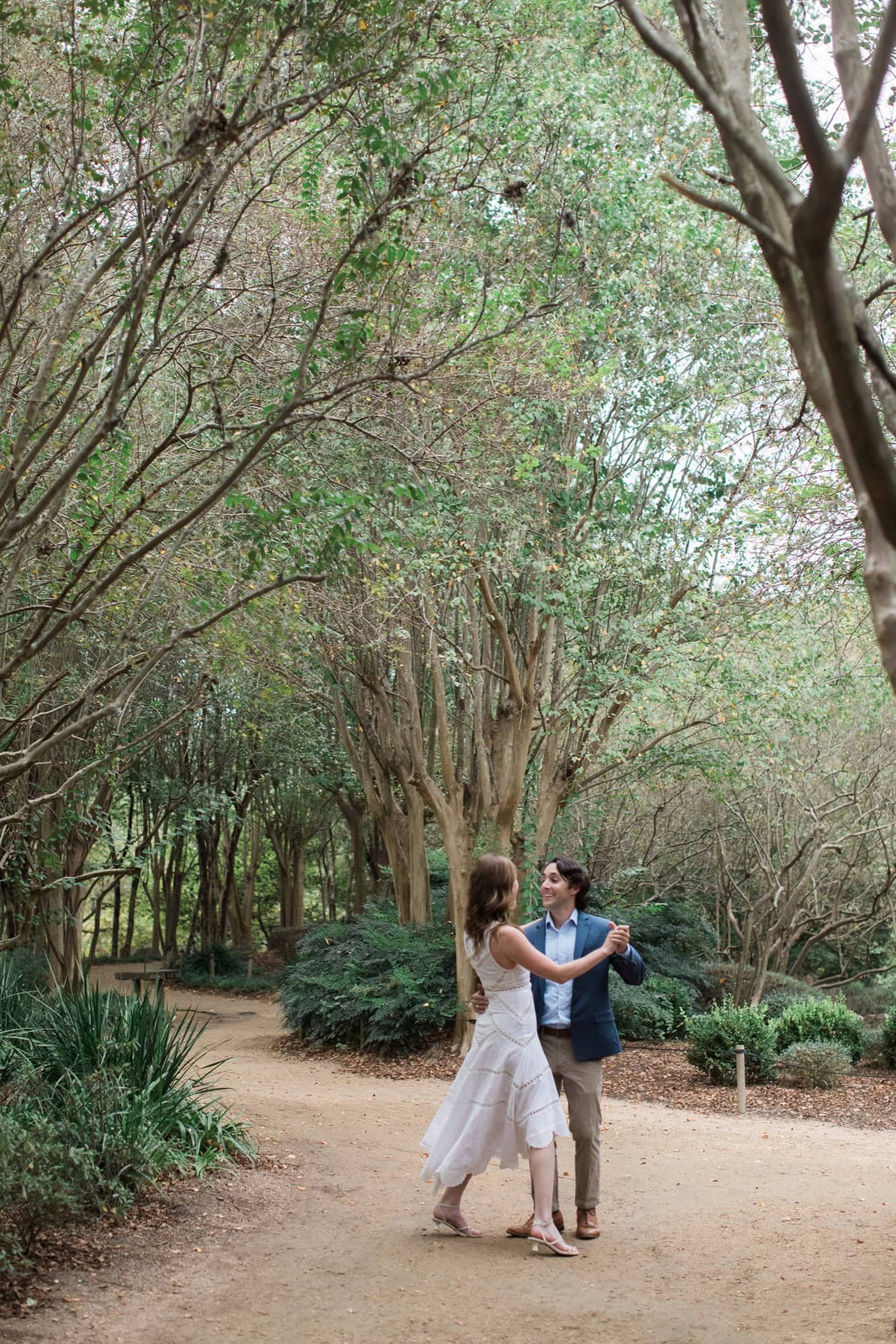 when should you take engagement photos Engaged couple dancing on a tree-lined garden path in Houston