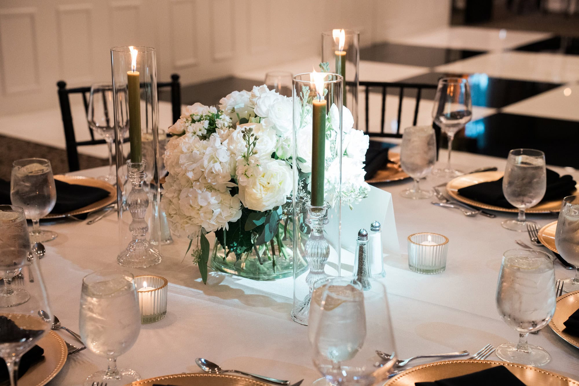 White floral centerpiece with tall green candles and gold chargers.